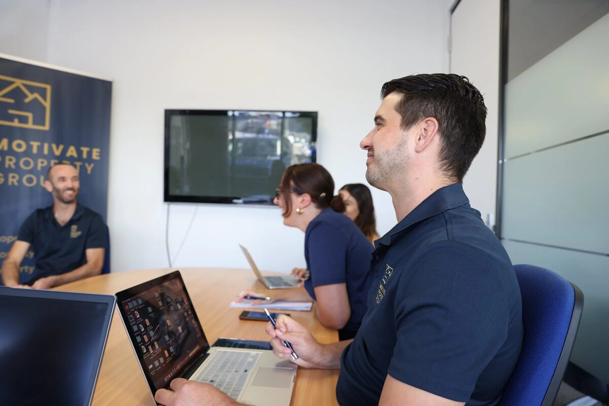 Motivate Property Group team members around a meeting table with laptops, the company banner behind them