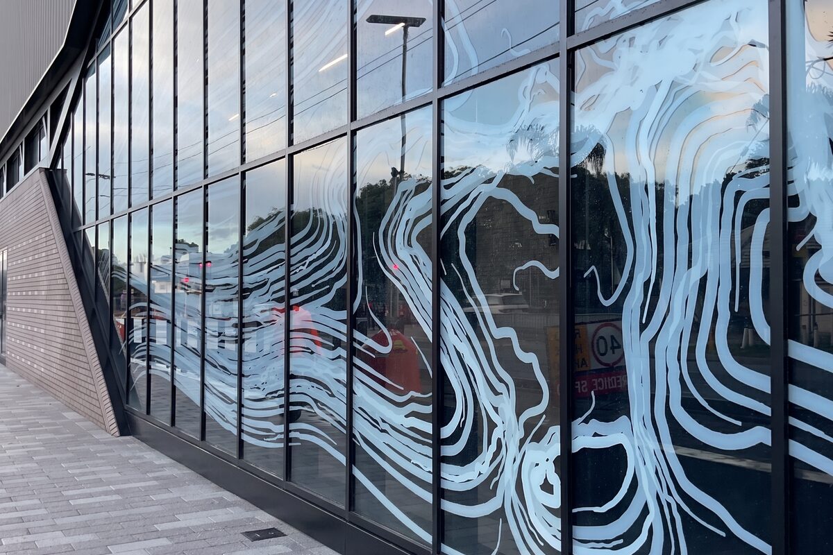 Digitally printed glass facade panels with white flowing line artwork on a METRONET Victoria Park-Canning station in Perth