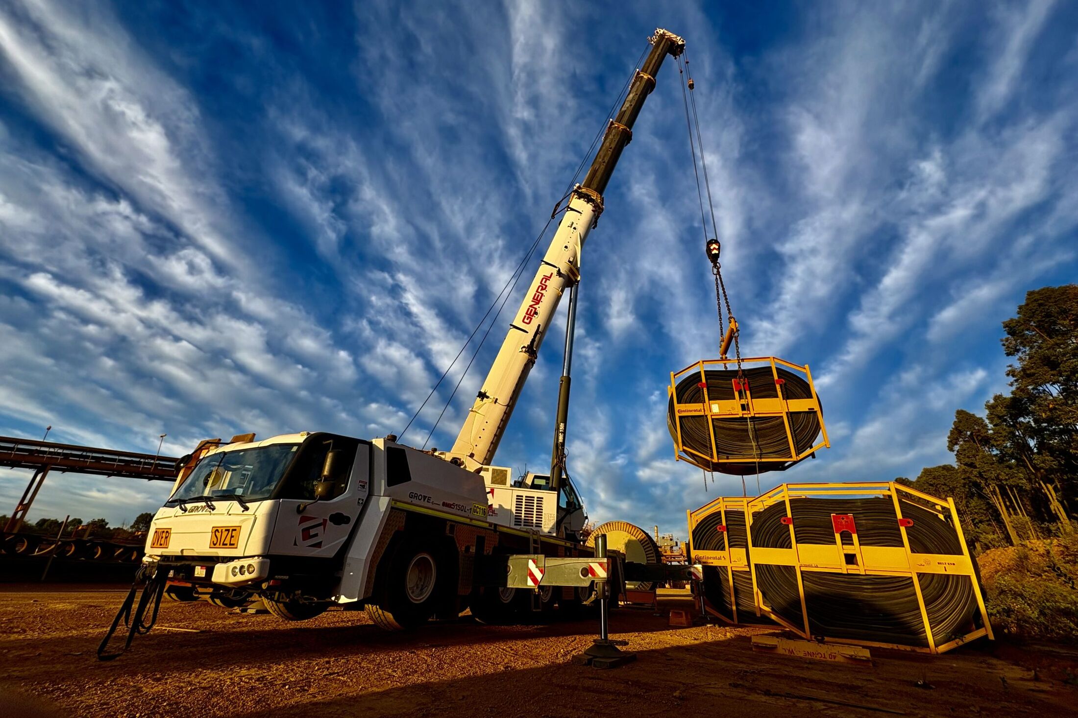 A General Crane Services mobile crane lifting conveyor belt reels at sunrise