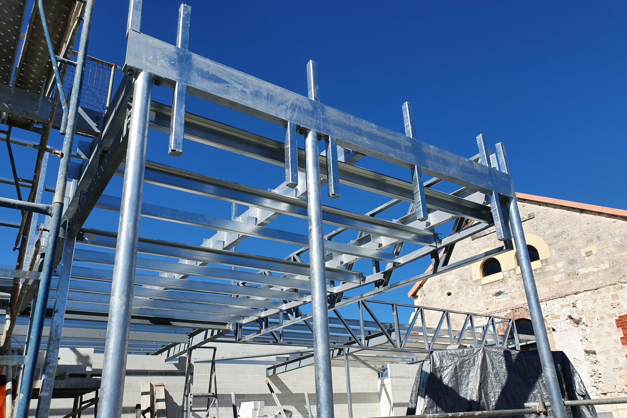 Galvanised steel framing against a blue sky beside the heritage stone walls of The Old Synagogue in Fremantle
