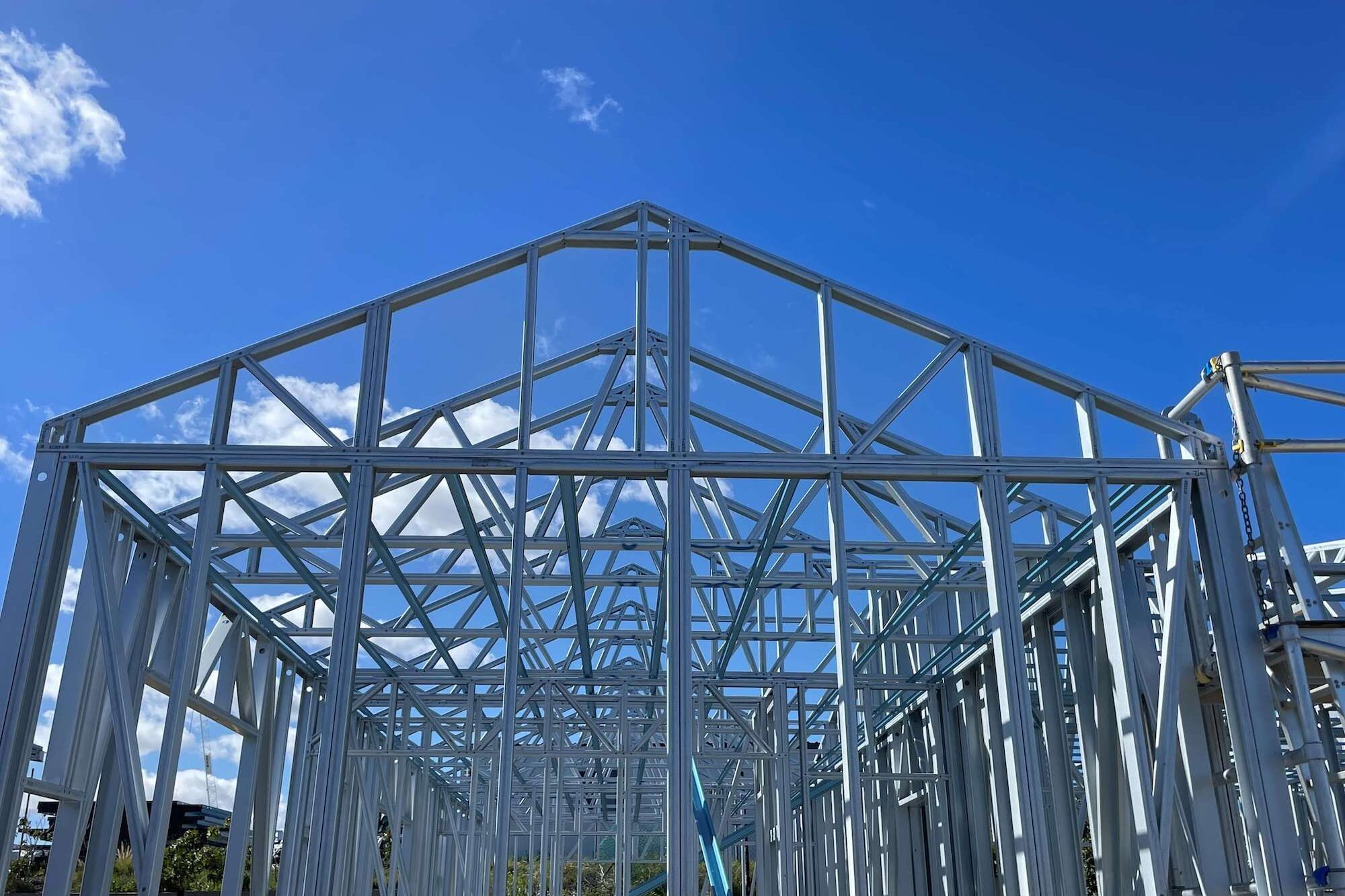 Light-gauge steel wall frames and roof trusses standing on a house site against a blue sky